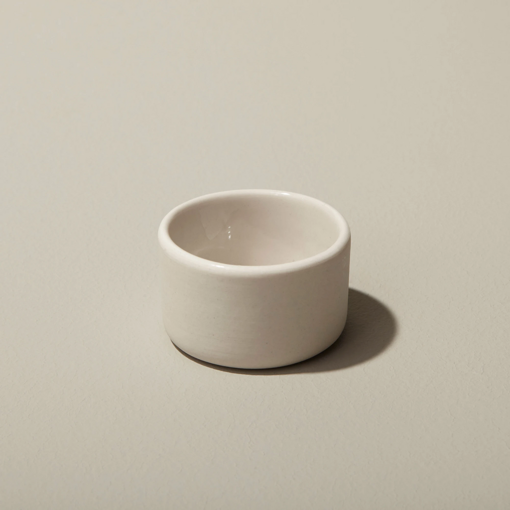 Small white stoneware cellar / bowl on a tan background.