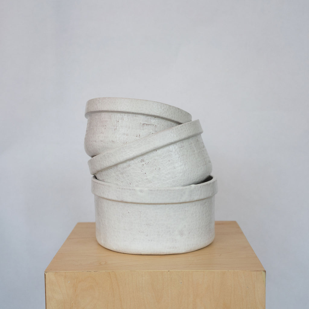 Stack of three white ceramic bowls on a wood platform in front of a white background.