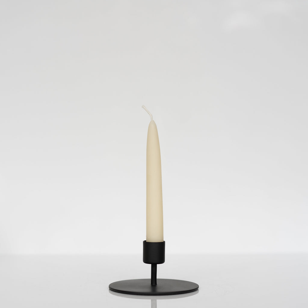 Short modern matte black taper candle holder holding an ivory taper candle.