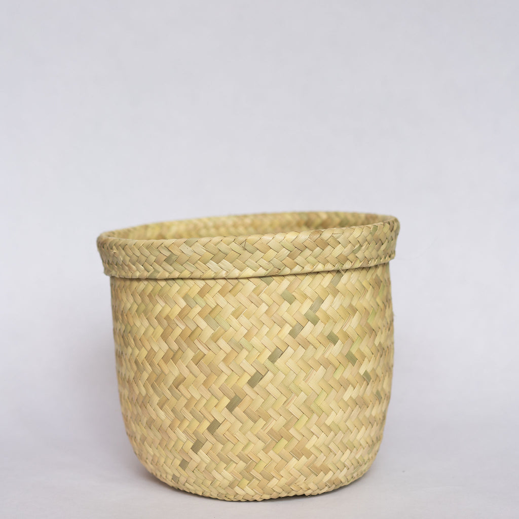 Short handwoven palm fiber straight sided basket in natural tan. Slight ridge around top. Gray background. 