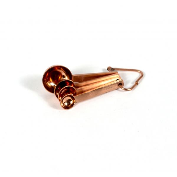 Matte copper measuring spoon set held together by copper metal triangle fanned out on a white background.