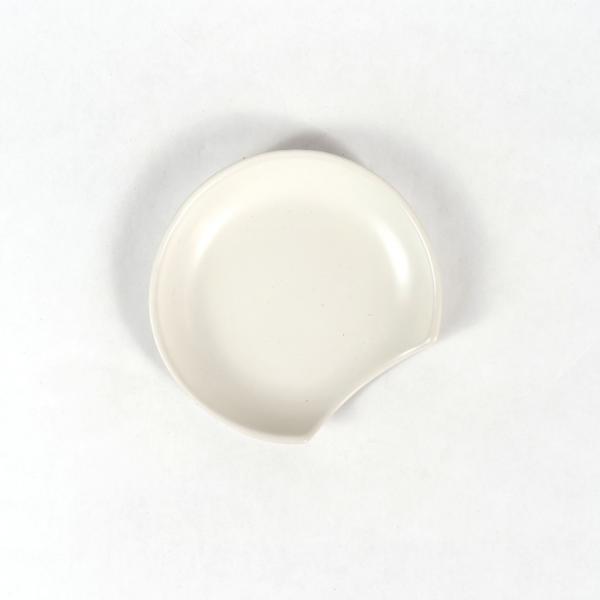 White stoneware notched round spoon rest on a white background.