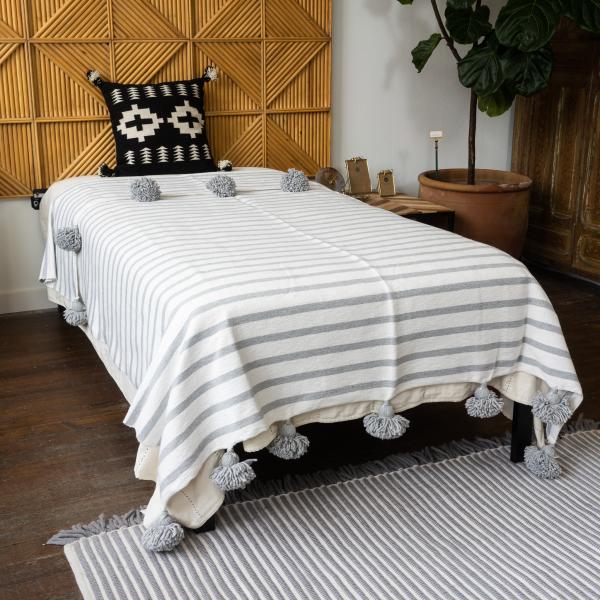Woven cotton gray and cream striped blanket is on twin bed in front of a geometric wood headboard.