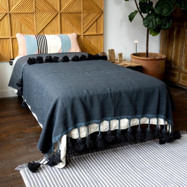 Woven cotton navy blanket is on twin bed in front of a geometric wood headboard.
