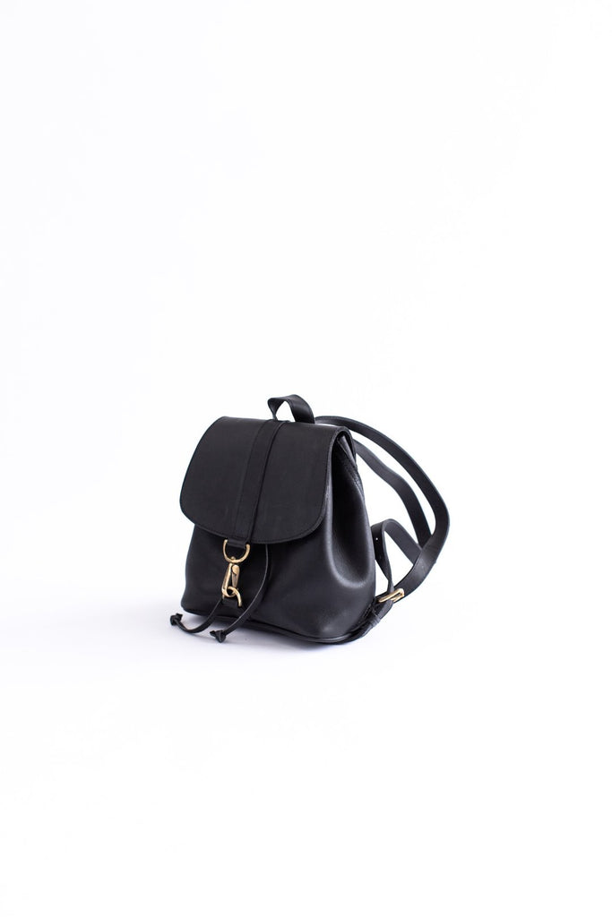Vegetable tanned black leather small backpack with gold clasp hardware sits on a white background.