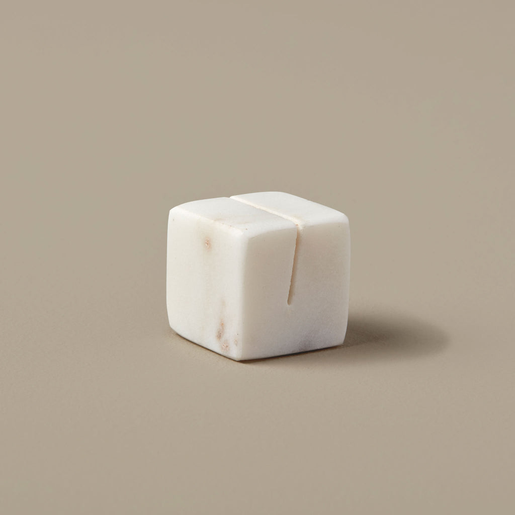 White marble cube shaped placecard holder sits against a tan background.