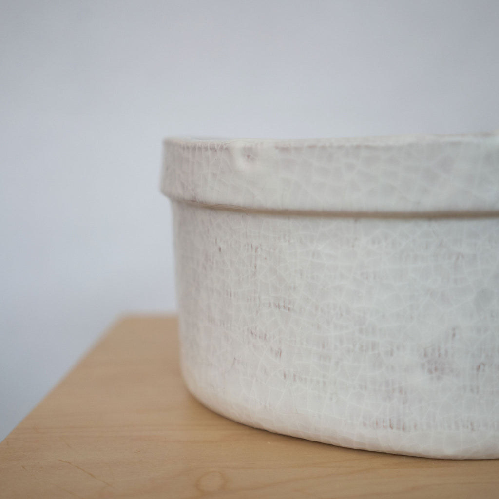Detail shot of the side of a white ceramic bowl on a wood platform in front of a white background.