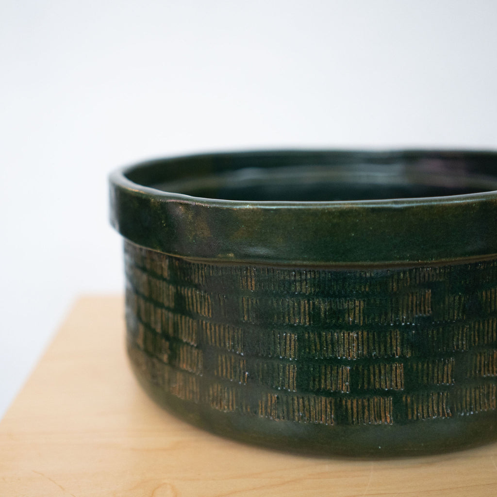 Detail shot of dark green ceramic bowl on a wood platform in front of a white background.