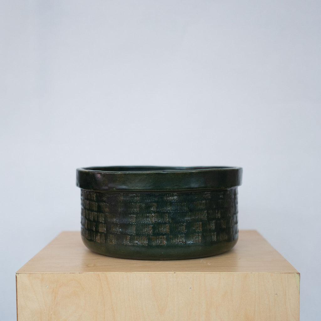 Large dark green ceramic bowl on a wood platform in front of a white background.
