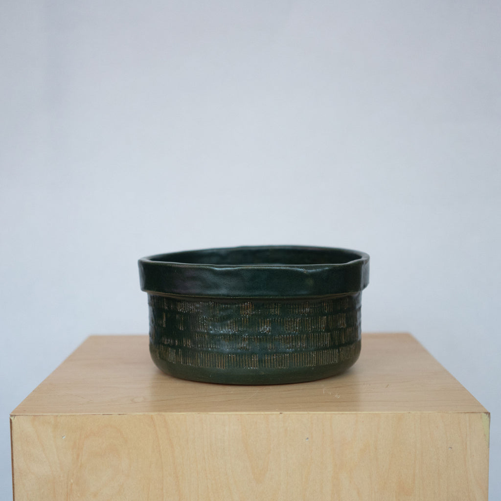 Medium dark green ceramic bowl on a wood platform in front of a white background.