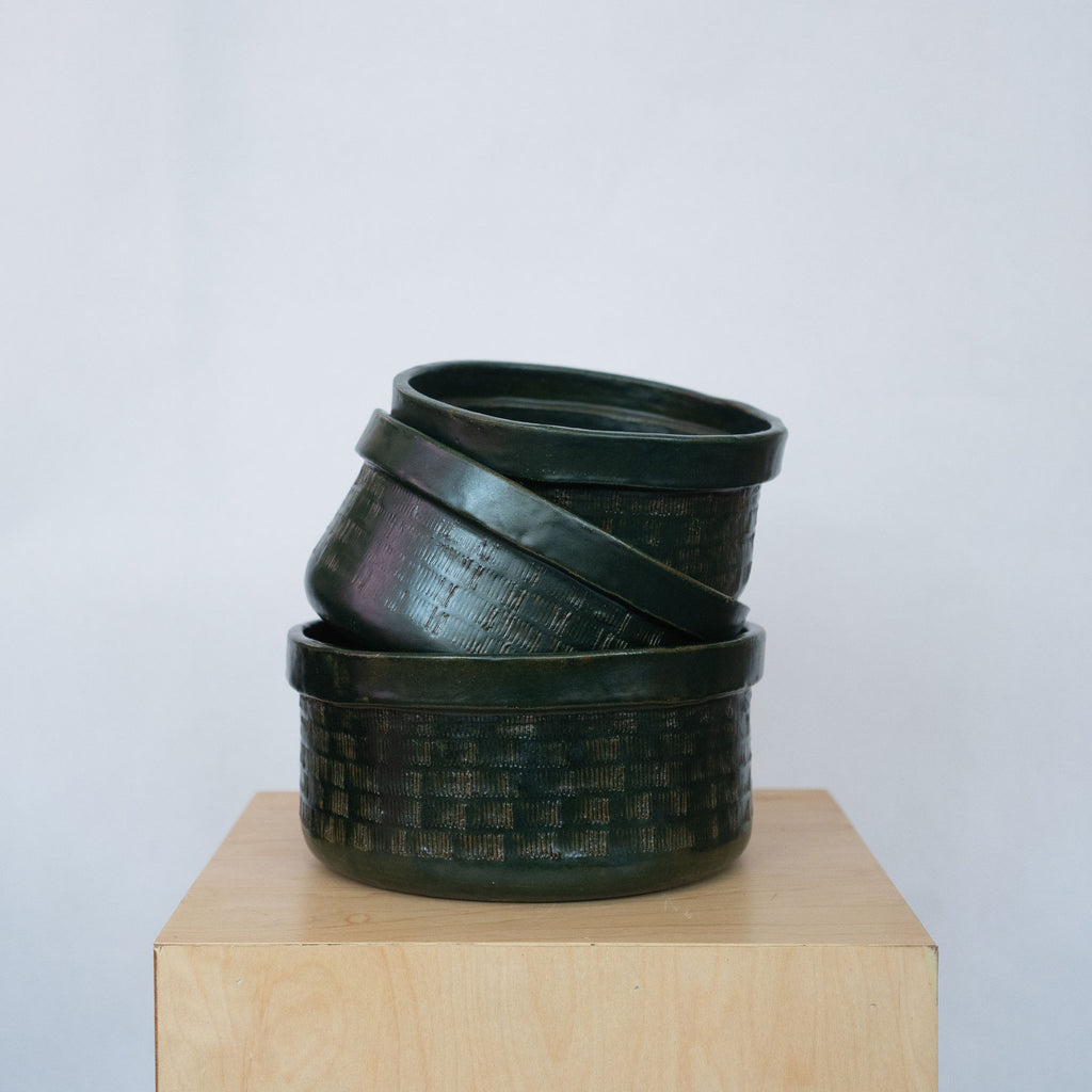 Stack of three dark green ceramic bowls on a wood platform in front of a white background.