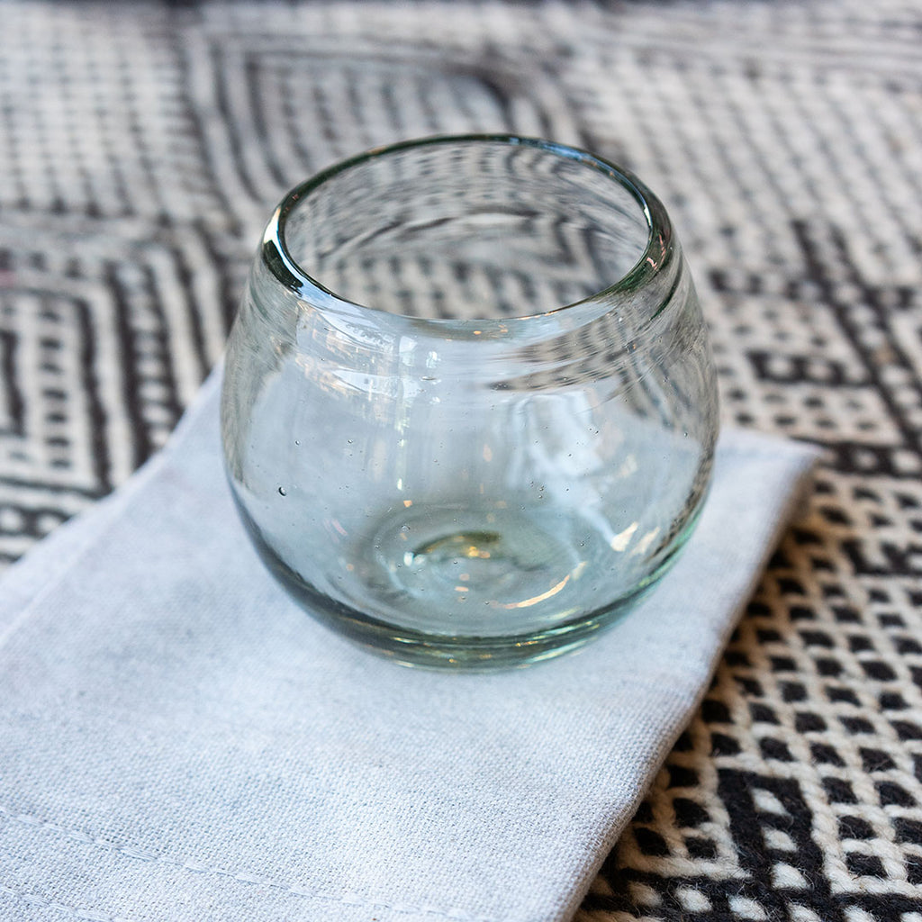 A round clear short handblown glass sits on a light gray tea towel on a geometric wool background.