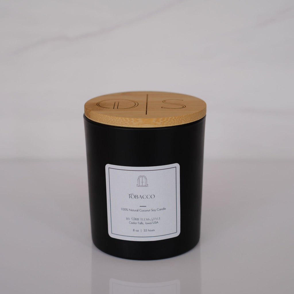 Matte black glass candle with a white square label and bamboo lid. Gray background.