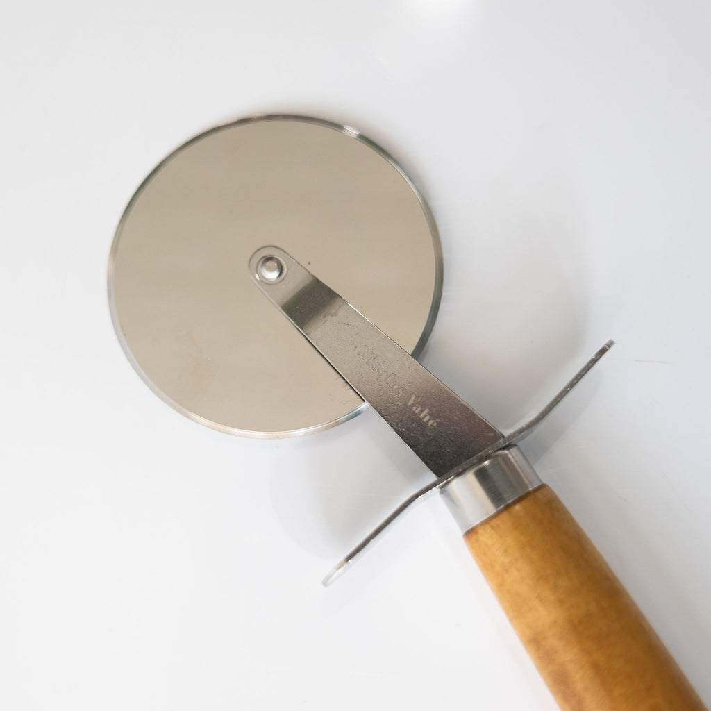 Stainless steel pizza cutter with acacia wood handle. Light gray background.