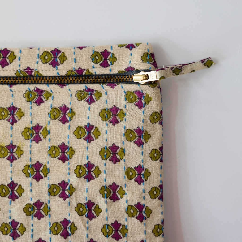 Close up of a zipper pouch clutch that is handmade and embroidered with the traditional Kantha stitch over recycled sari fabric in cream and olive green and orchid purple floral pattern. White background.