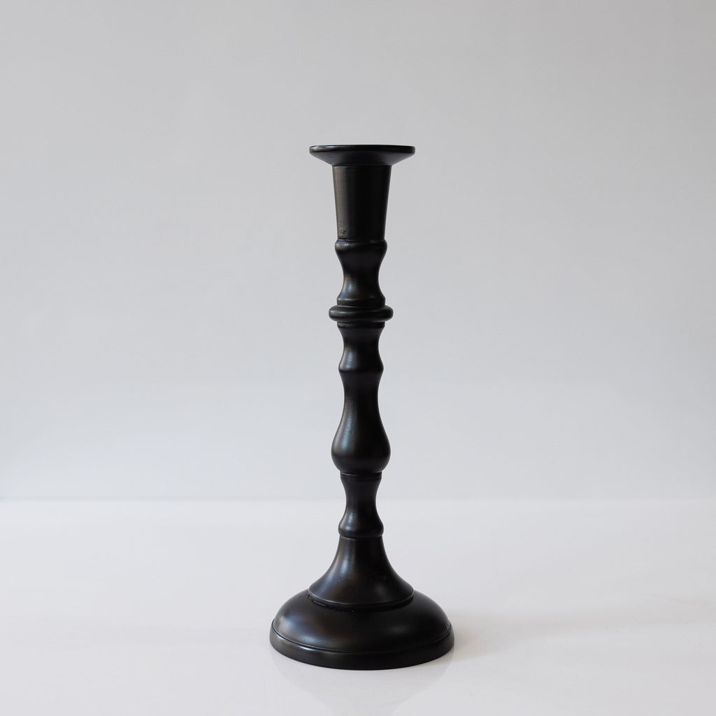 One hand turned black taper candlestick on white background.