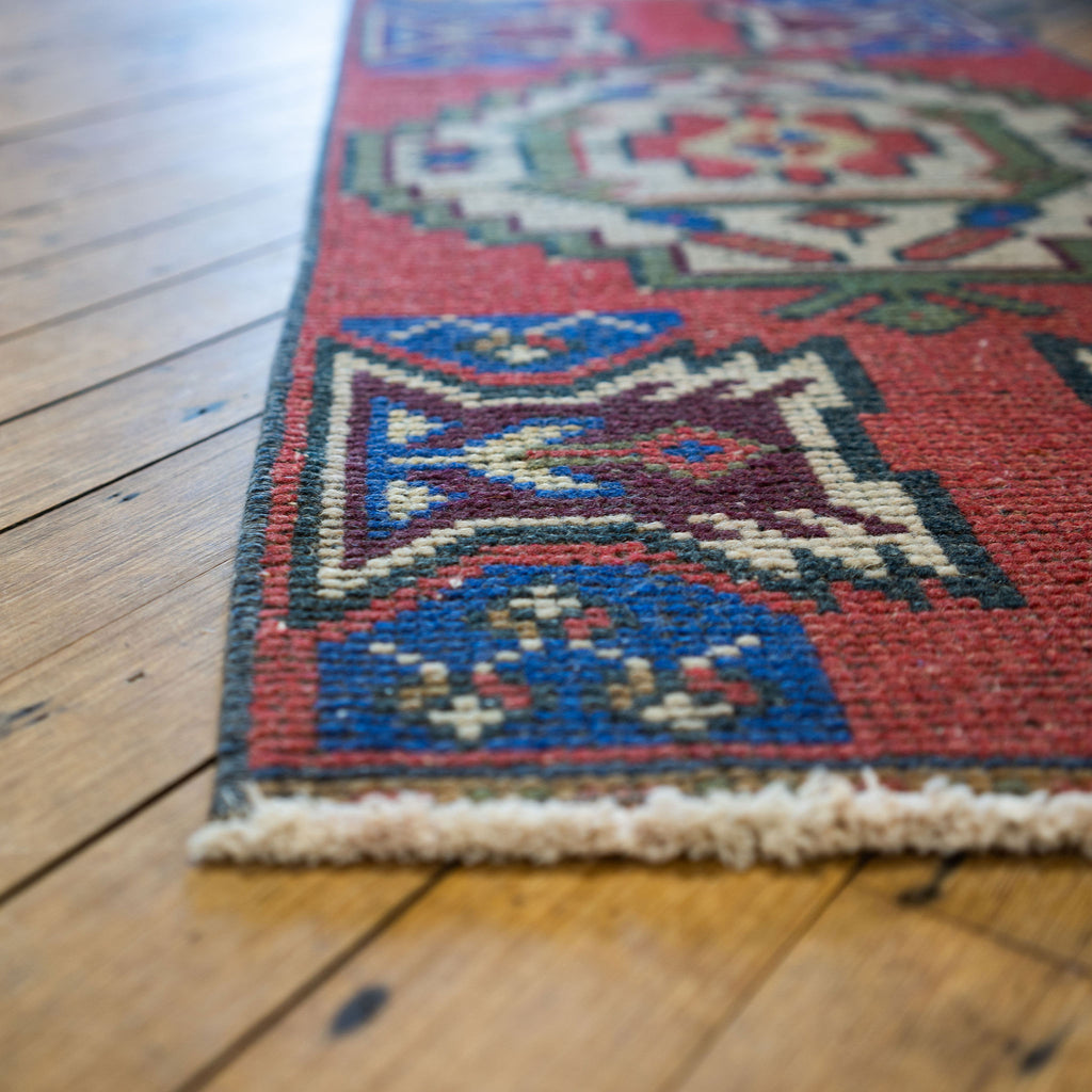 Close up of a small vintage Turkish rug with classic bold geometric design in red, green, blue, cream, maroon, and pale yellow.