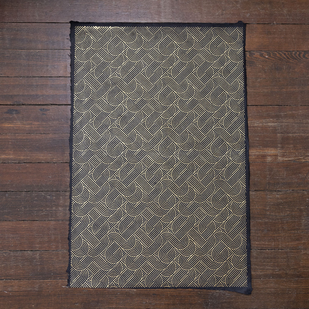 Handmade and printed paper gift wrap. Pattern is repeat art deco gold geometric design on black background.