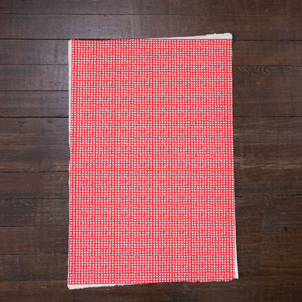 Handmade and printed paper gift wrap. Pattern is small red grid on cream background.