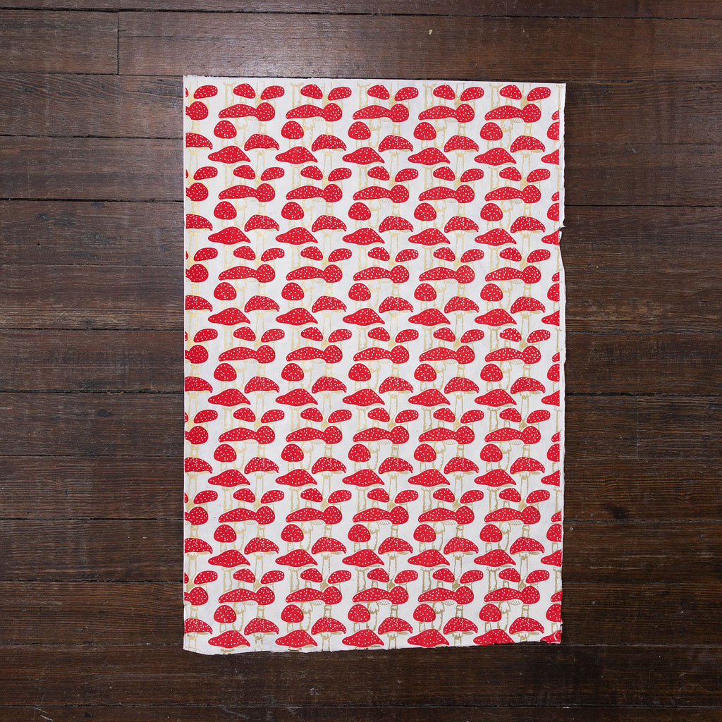 Handmade and printed paper gift wrap. Pattern is repeat red mushrooms on white background.