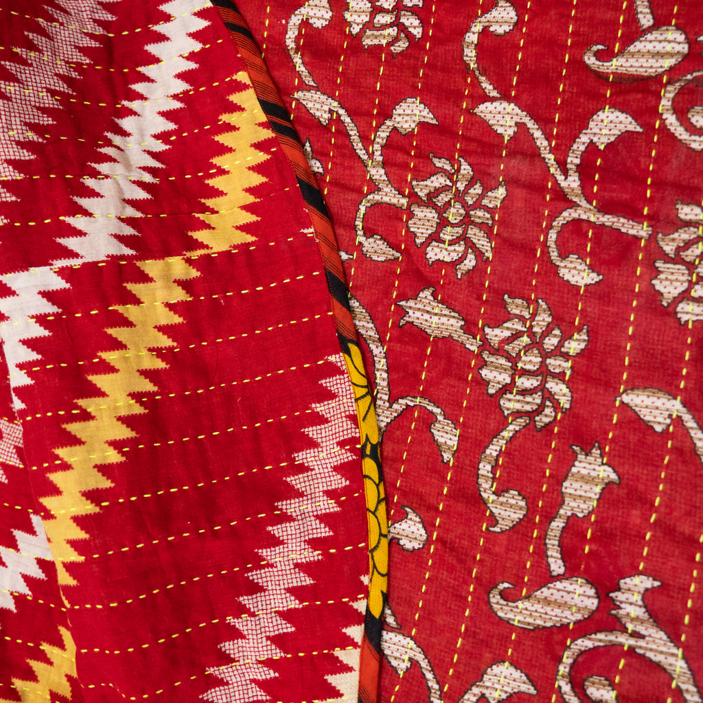 A tree skirt that is handmade and embroidered with the traditional Kantha stitch over recycled sari fabric in primarily cream and red with yellow accents. Reversible with one side featuring a floral pattern and the other side a zig zag pattern. 