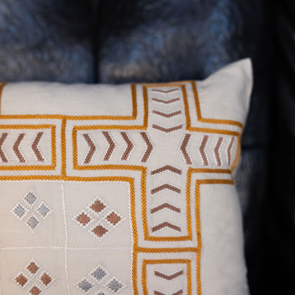 Embroidered cream lumbar pillow featuring Tarshumar design embroidery, with symmetrical crosses and small arrows and small diamonds. Detail shot.