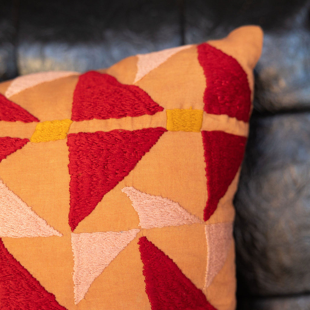 Embroidered tangerine colored square pillow with red + peach arrow design with orange dashes. Close up.