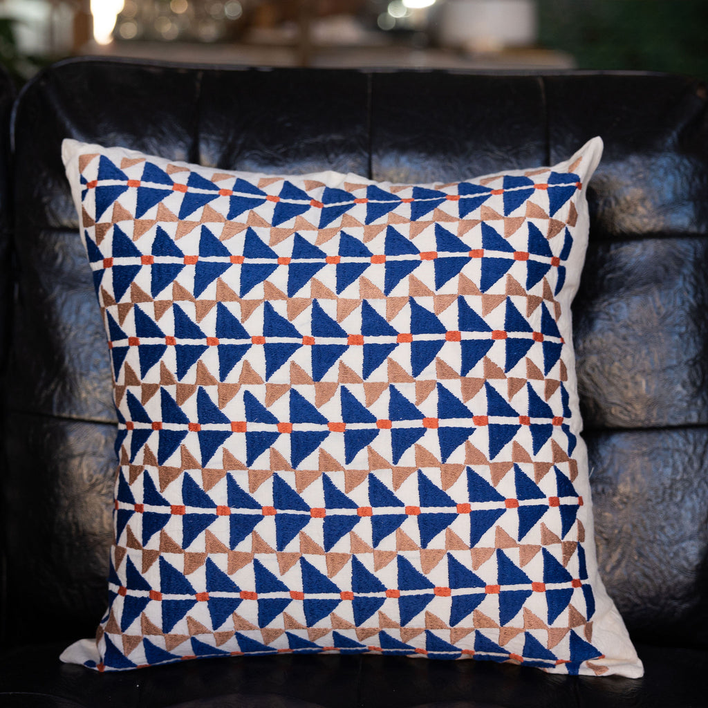 Square pillow featuring Puktadozi style embroidery with blue + tan triangles and orange dashes. 
