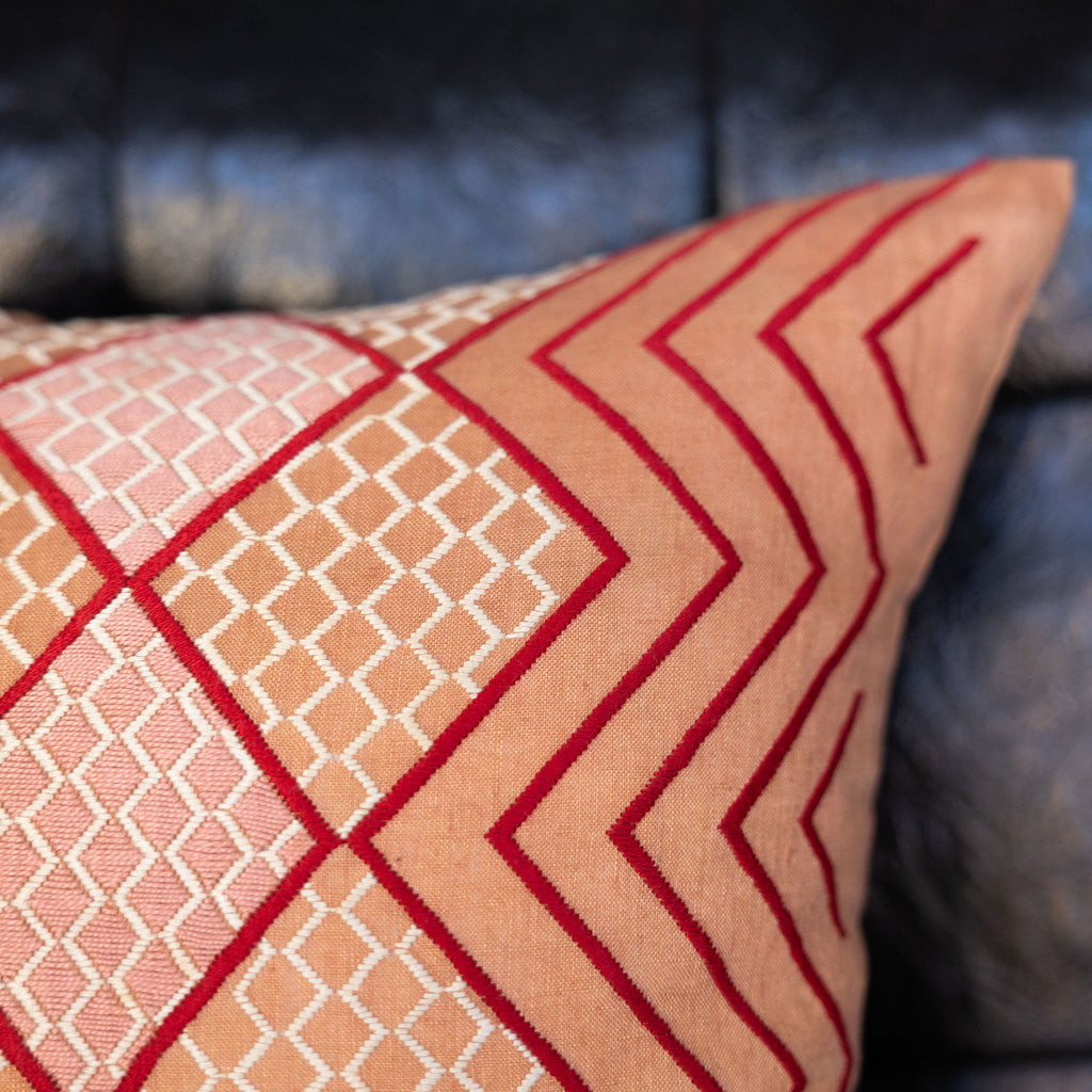 Embroidered tangerine square pillow featuring red zig zag and blush pink and cream diamond embroidery. Close up.