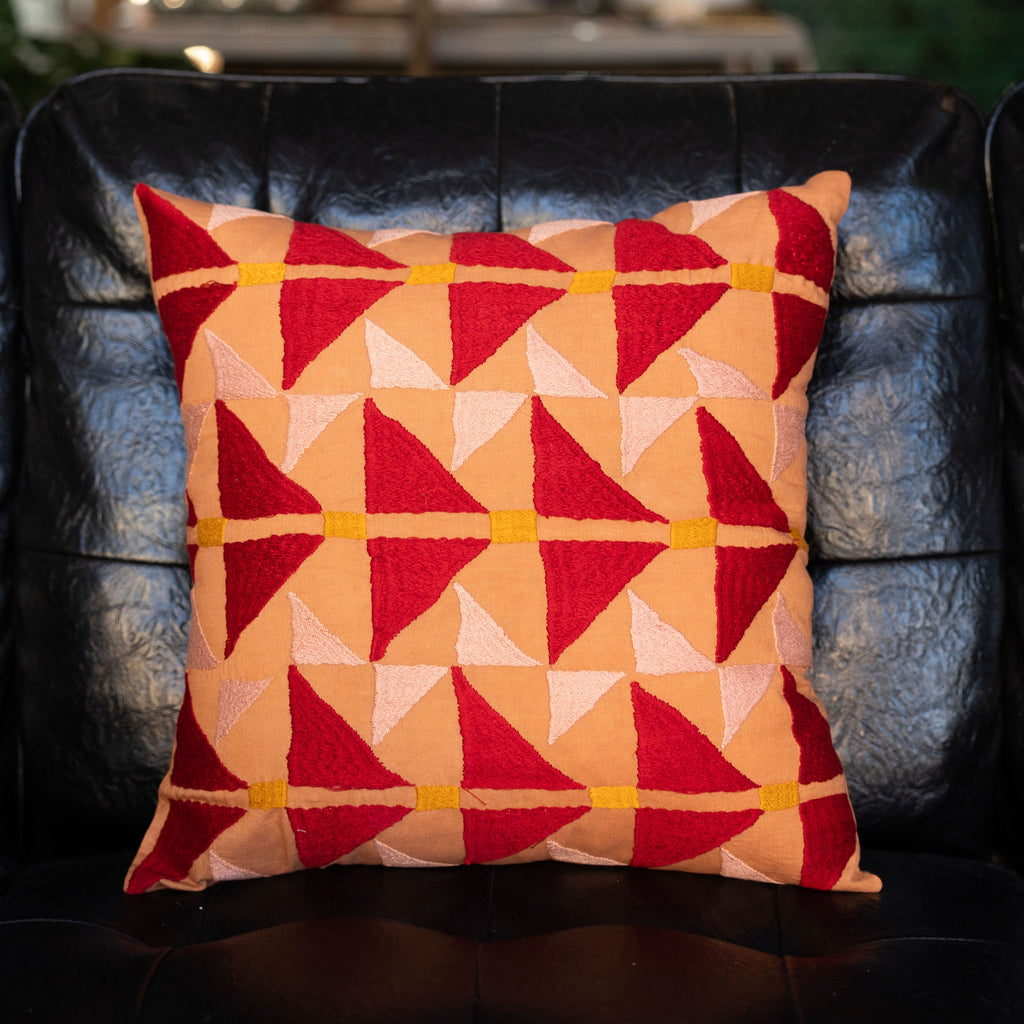 Embroidered tangerine colored square pillow with red + peach arrow design with orange dashes.