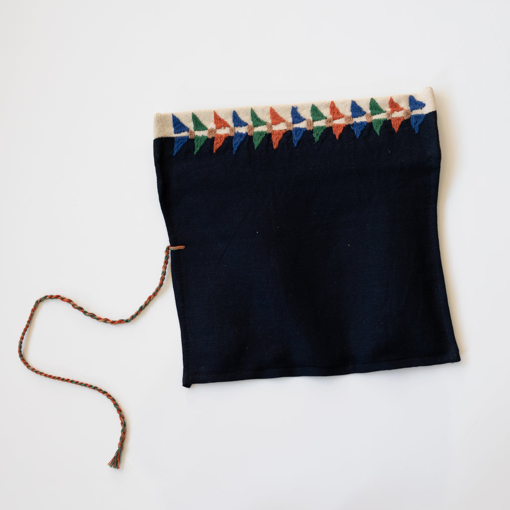 Embroidered roll up pencil case. Black and tan with blue,  orange, green, tan embroidery. Laying to showcase back with triangle embroidery.