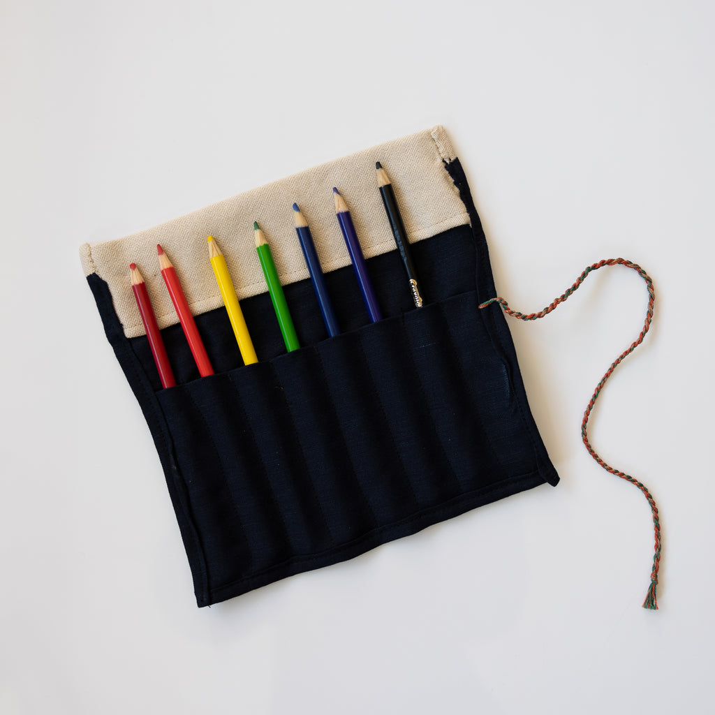 Embroidered roll up pencil case. Black and tan with blue,  orange, green, tan embroidery. Shown laying open with colored pencils inside slots.