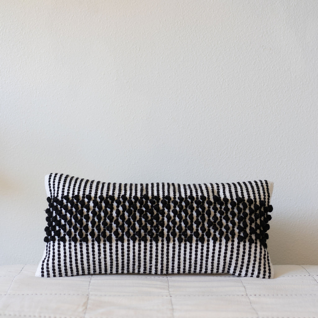 Rectangle cream wool pillow with a woven black striped design with a wide stripe of poms through the middle.