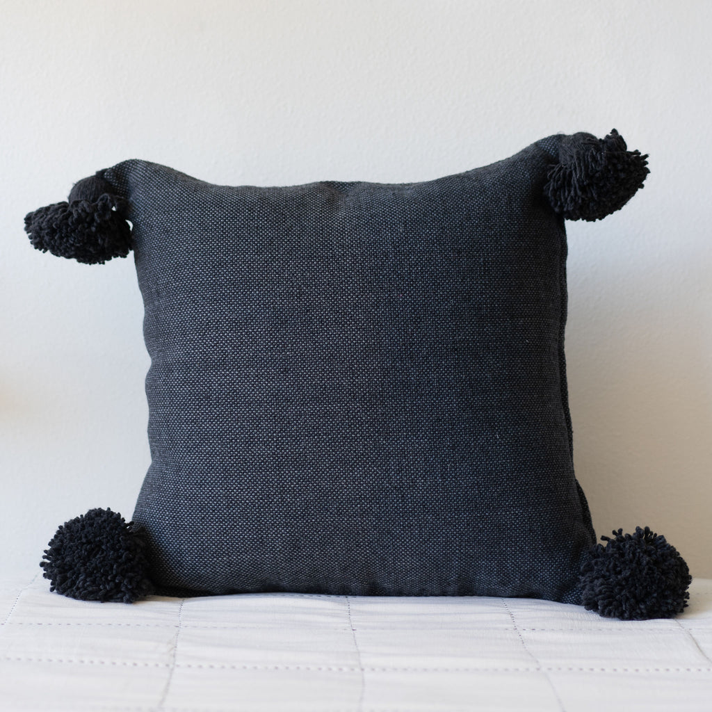 Square woven cotton navy blue pillow and big poms at each corner.
