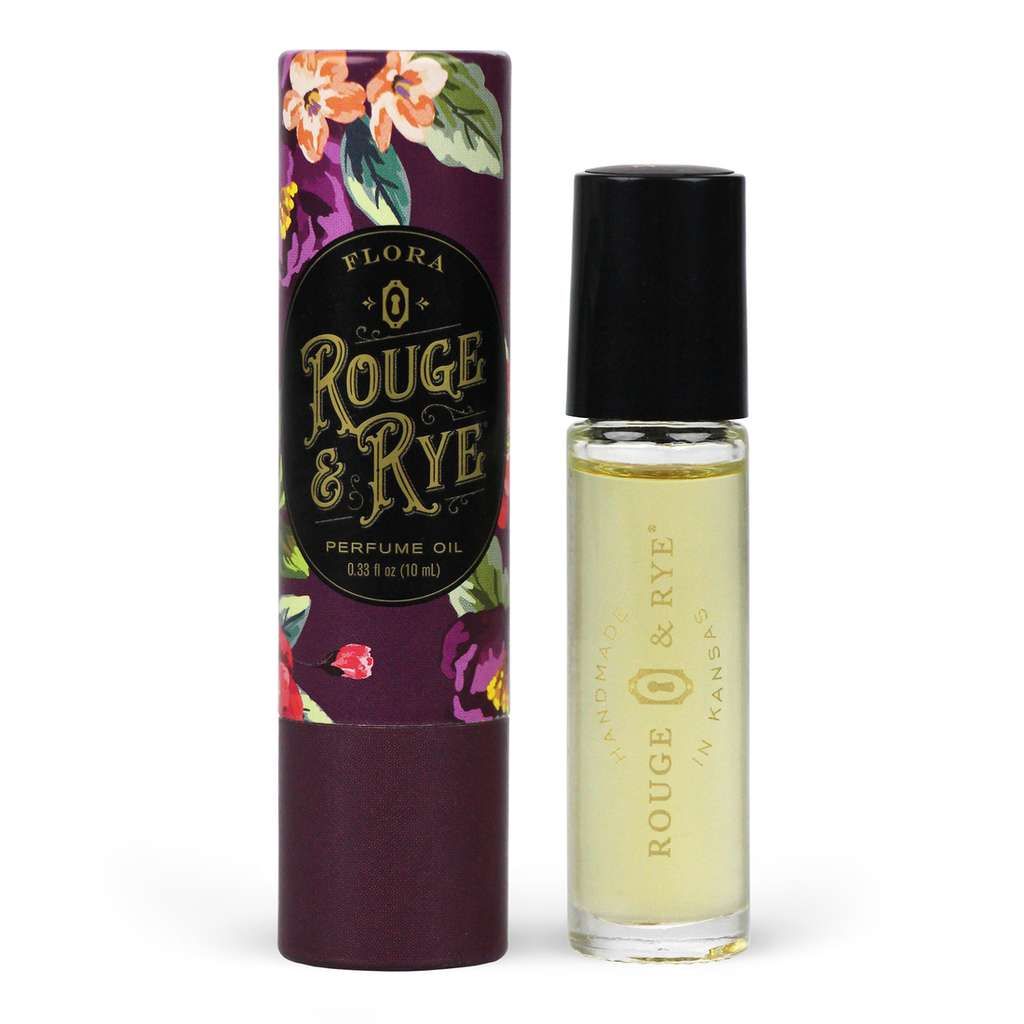 Golden Flora perfume oil roller in clear glass bottle with black plastic cap next to purple floral packaging. White background.