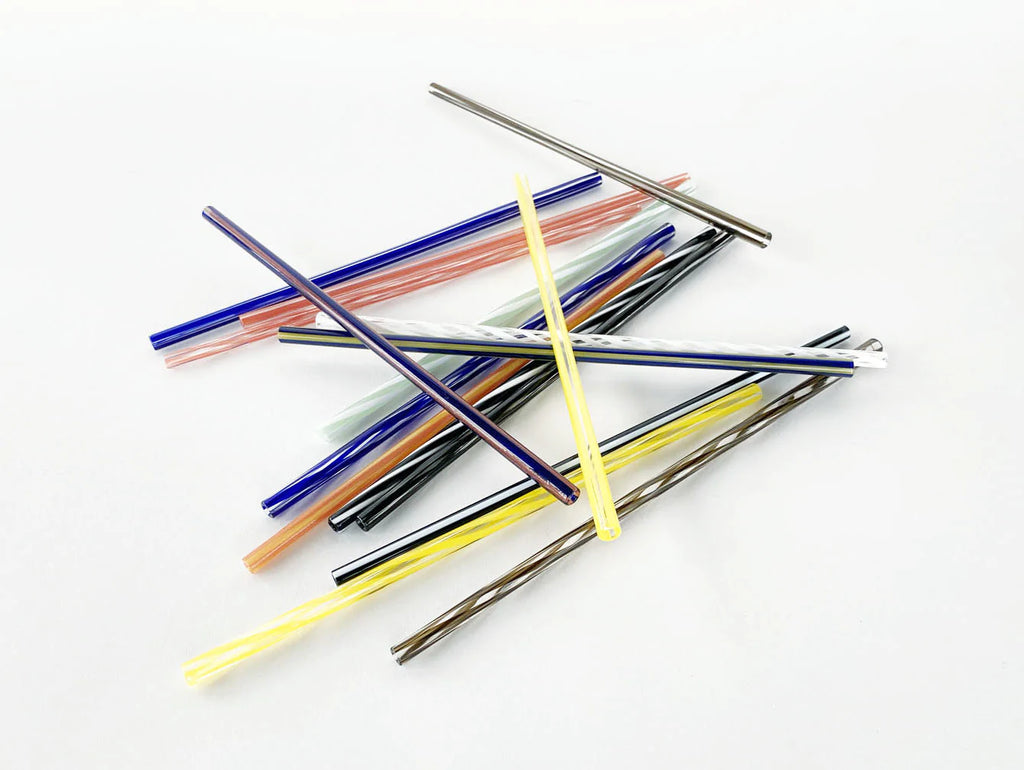 A pile of glass straws in many colors. Blue, coral, yellow, brown, black.