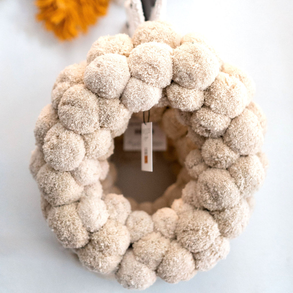 Wreath made entirely from cream wool pom poms. White background.