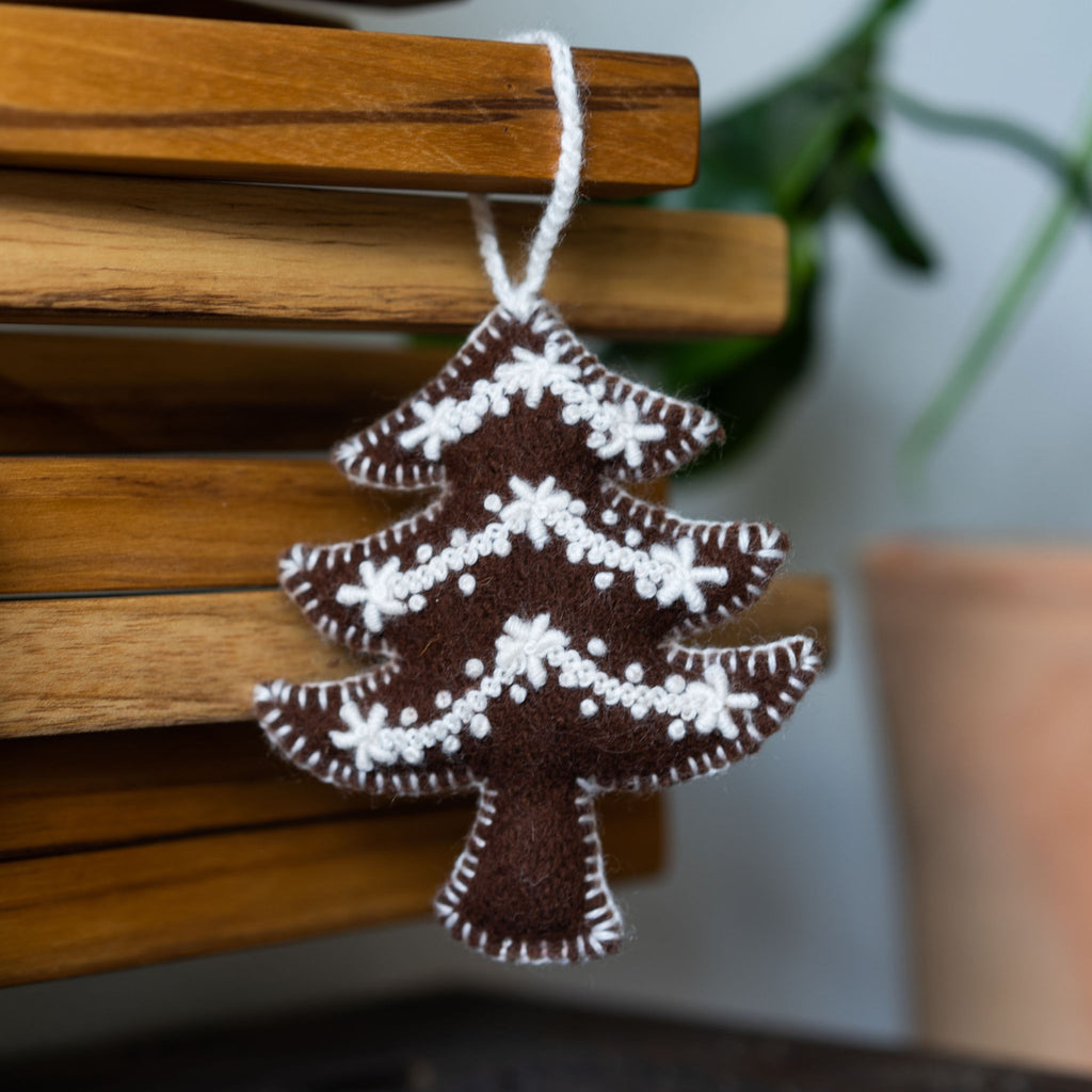 Wool Christmas tree ornament in the shape of a Christmas tree. Brown with cream embroidery. Wood background.