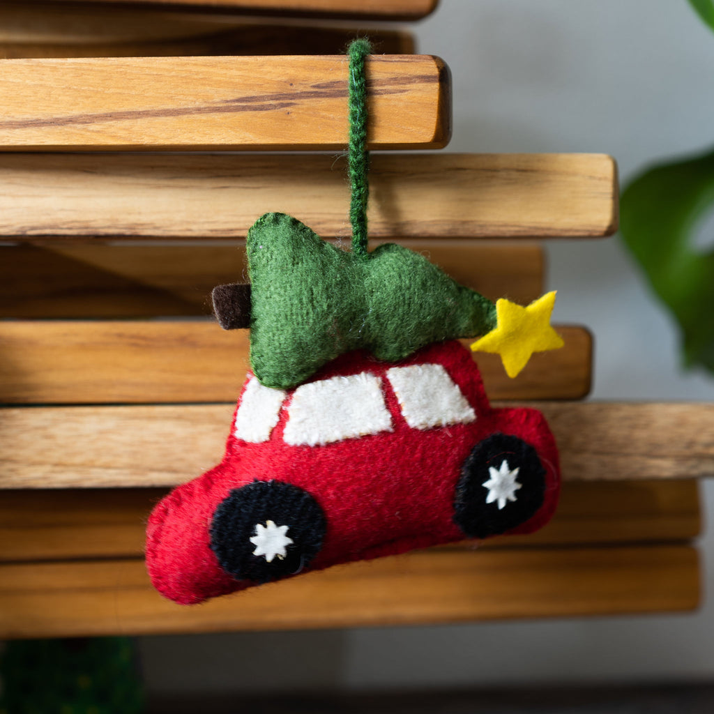 Wool tree ornament shaped like a red car with Christas tree on top. Hangs in front of a wood background.
