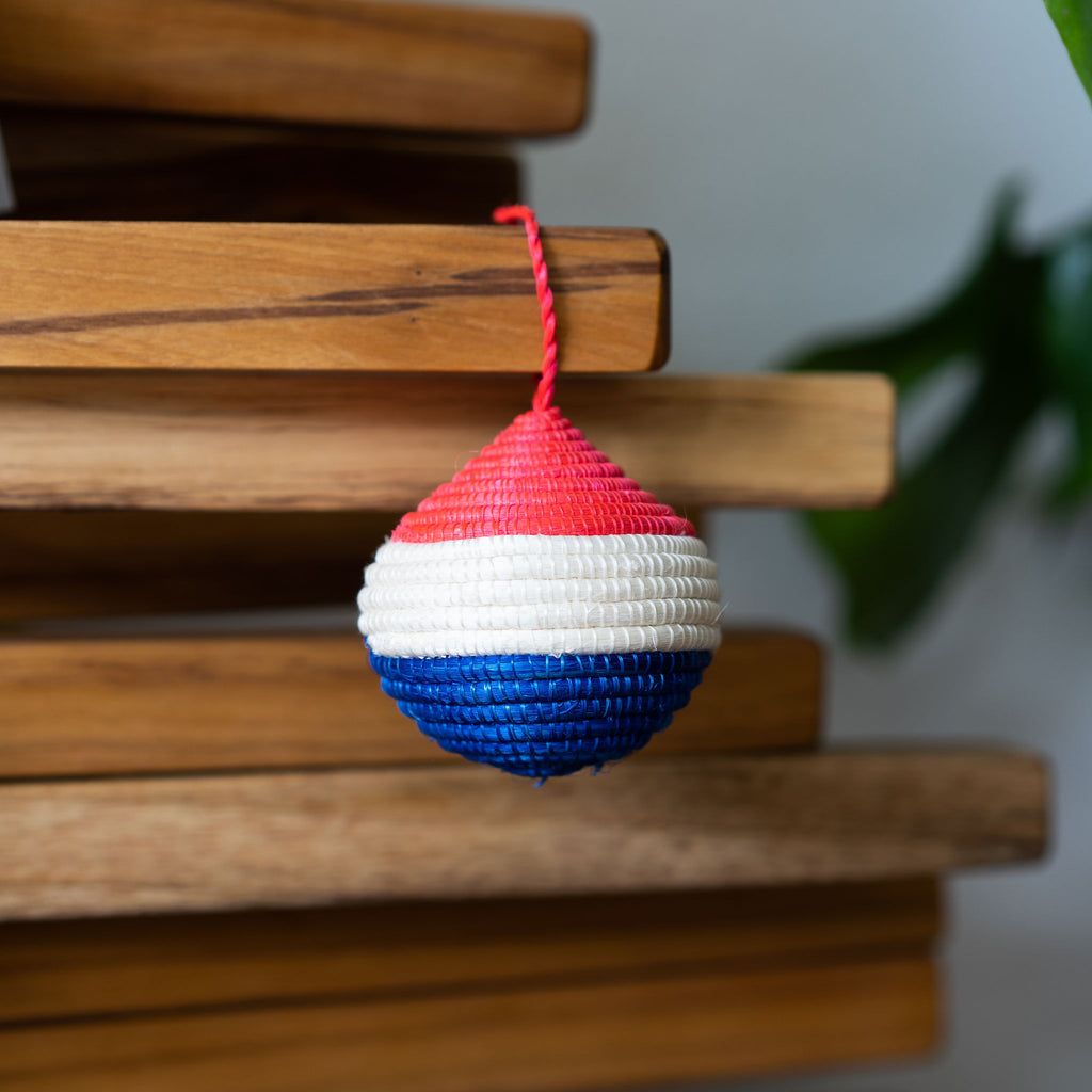 Handwoven round red, white, and blue sweetgrass Rwandan tree ornament. Wood background