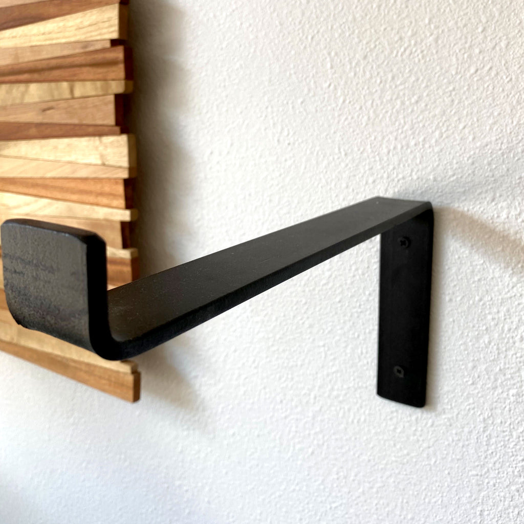 Black iron Z shelf bracket on a white wall next to a piece of wood artwork.