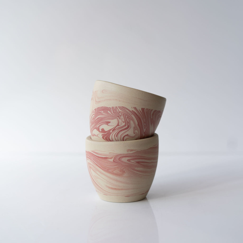 Stack of two pink marbled ceramic cups.