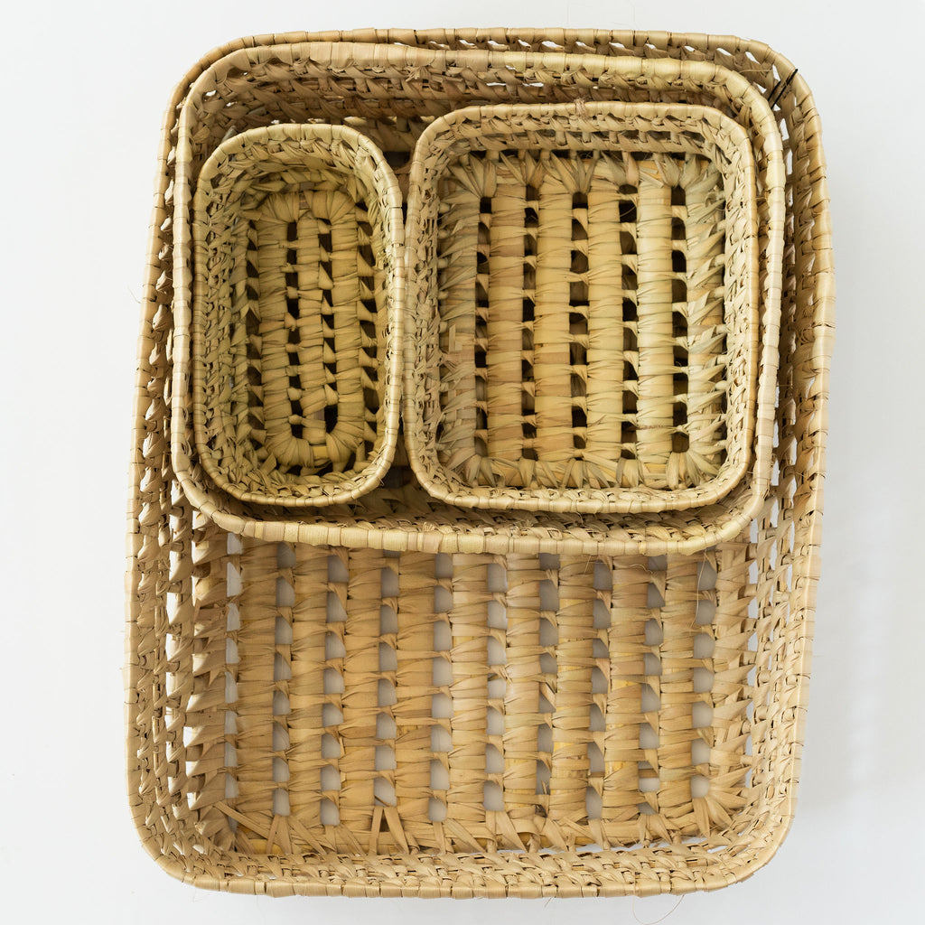 Set of four palm fiber baskets nested together. White background.