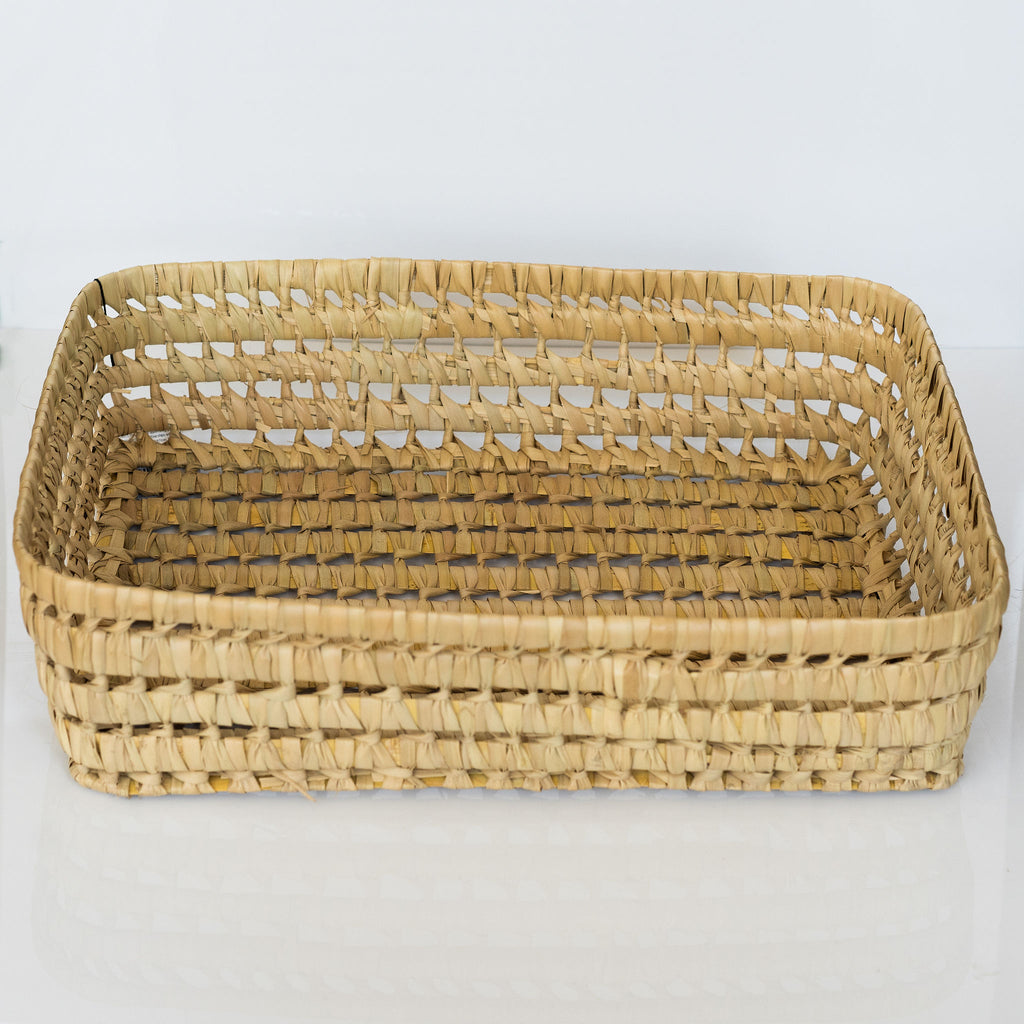 Large palm fiber loosely woven rigid basket sits against a white background.