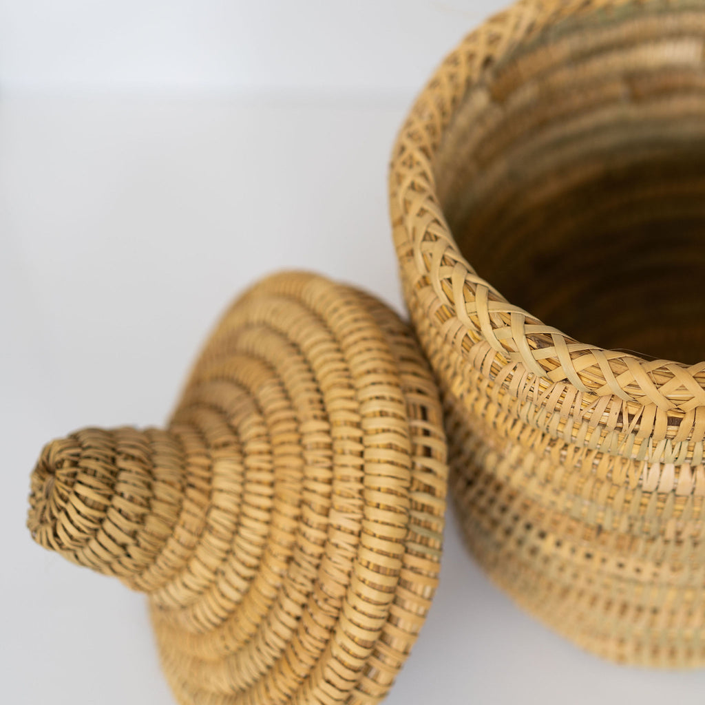 Small rush fiber handwoven basket with lid that has a knob handle. Light gray background.