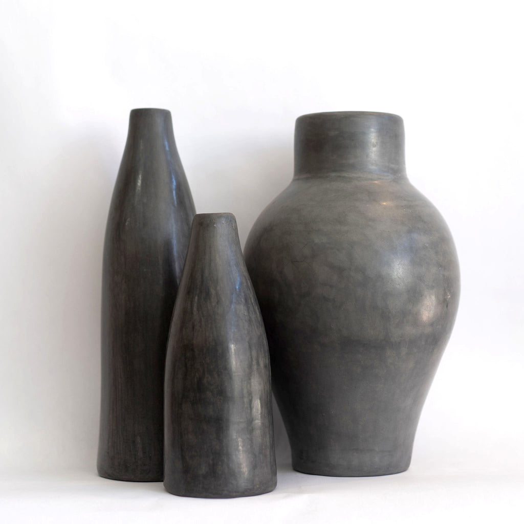 Group of three different sized and shaped dark gray Tadelakt vases. White background.