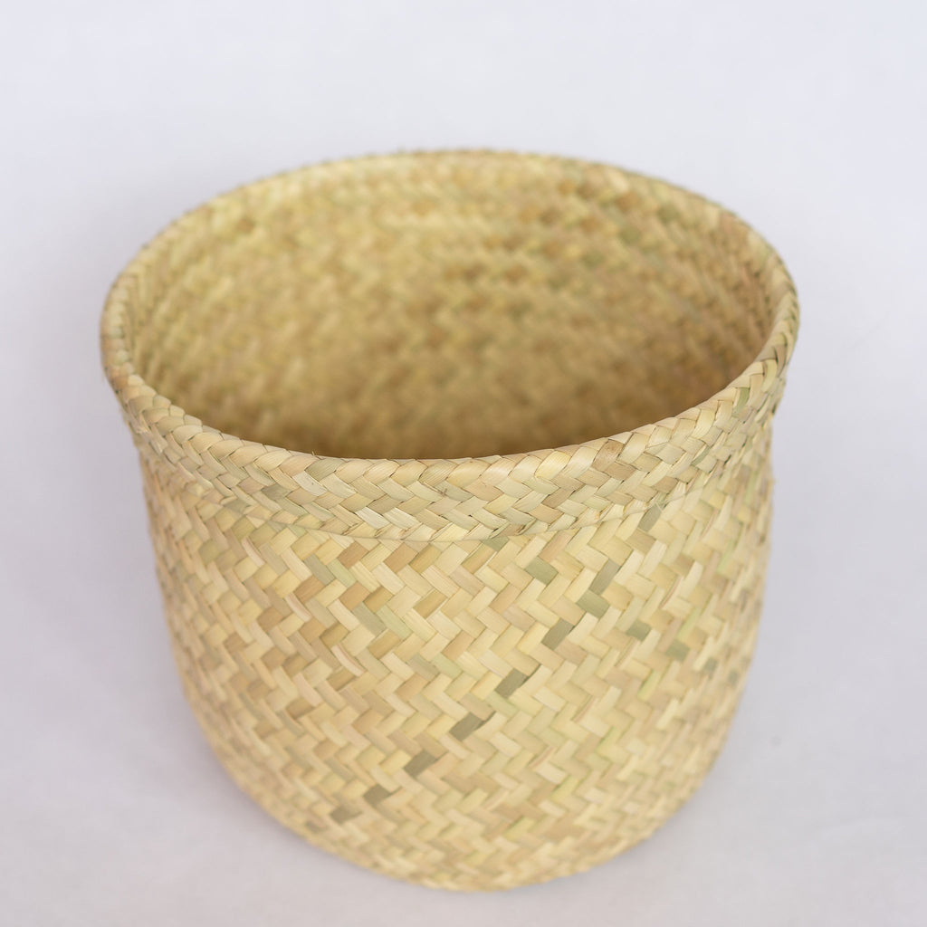 Short handwoven palm fiber straight sided basket in natural tan. Slight ridge around top. Interior is natural tan. Gray background. 