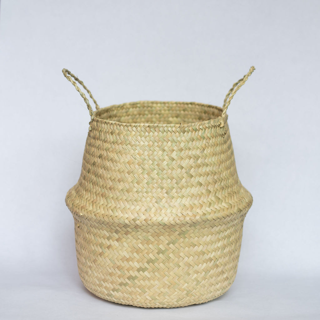 Handwoven palm fiber belly basket with handles in natural tan. Gray background.