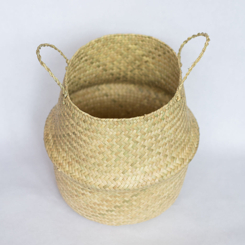 Handwoven palm fiber belly basket with handles in natural tan. Gray background.