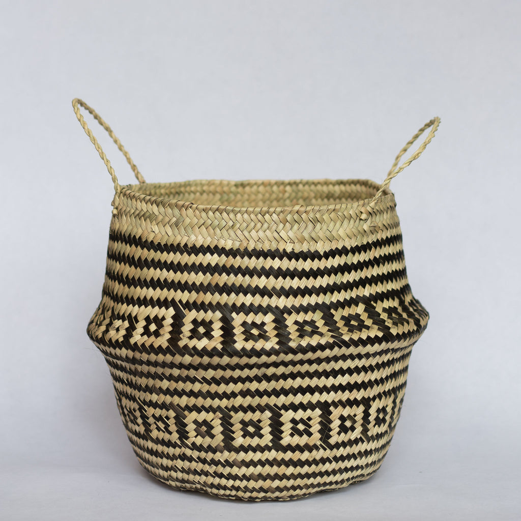 Handwoven palm fiber belly basket with handles in traditional Oaxacan designs. Tan and black stripes alternate with rows of contrasting layered squares. Gray background. 